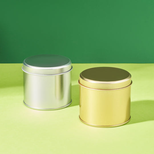 Tall round welded side seam tins in gold and silver on a green background. 