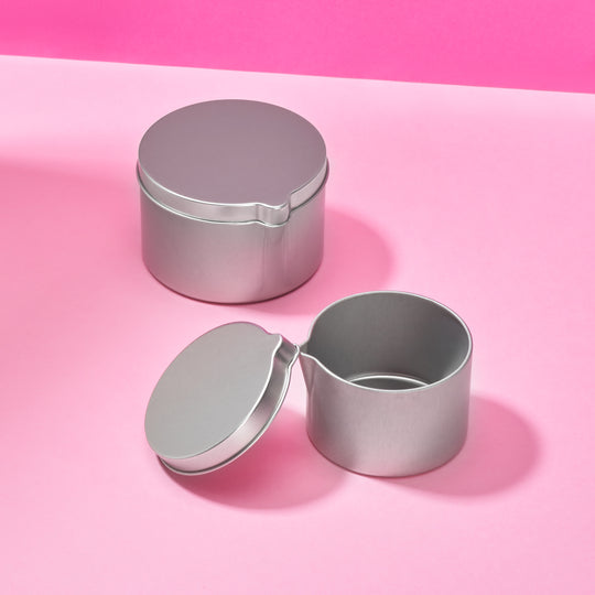 Seamless tins in silver with a pouring spout. Two tins shown, one with the lid off.